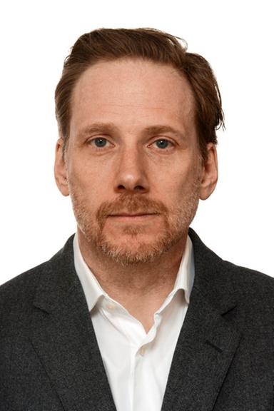 Der Publizist Björn Vedder, im grauen Sakko und offenem weißem Hemd, schaut freundlich in die Kamera.