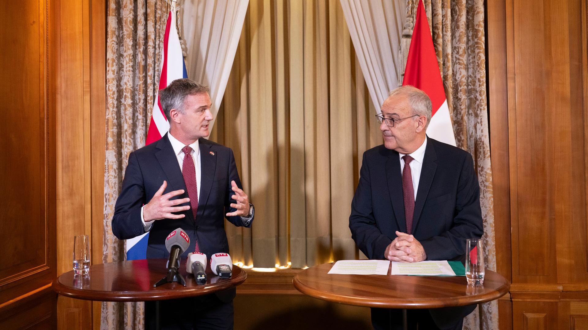 Der britische Handelsminister Kyle und der Schweizerische Bundespräsident Parlemin stehen an Rednerpulten nebeneinander.