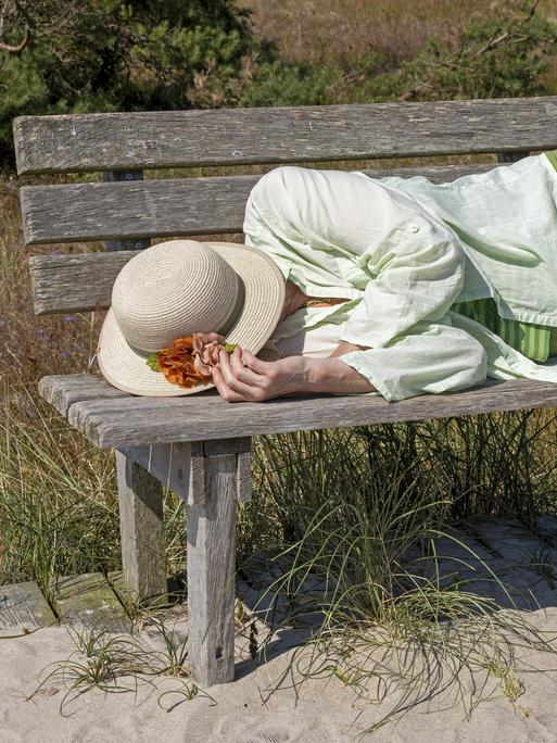 Eine ältere Frau schläft auf einer Sitzbank. 