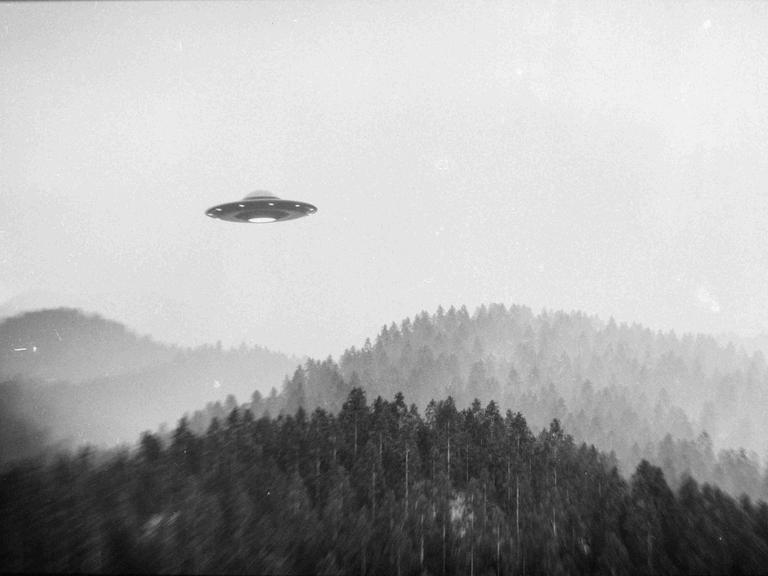 Schwarz-Weiß-Bild: Ein fliegendes Ufo über einer Waldlandschaft. Schwarz-Weiß-Bild: Ein fliegendes Ufo über einer Waldlandschaft.