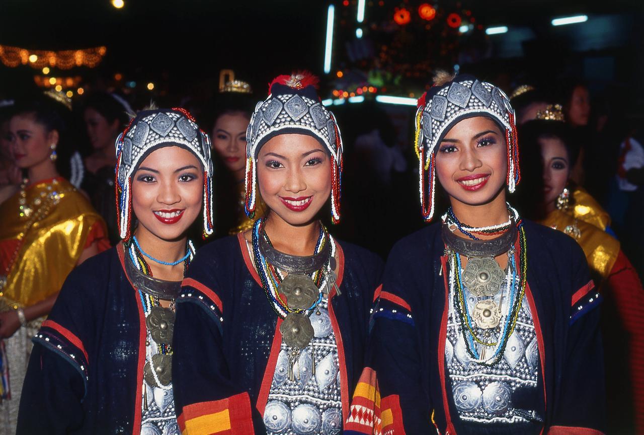Drei festlich gekleidete junge Damen mit Kopfbedeckung und roten Lippen.
