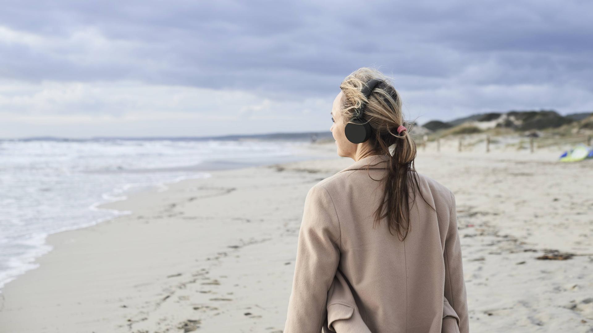 Eine Frau hört mit Kopfhörern am Strand Musik.