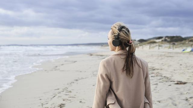 Eine Frau hört mit Kopfhörern am Strand Musik.