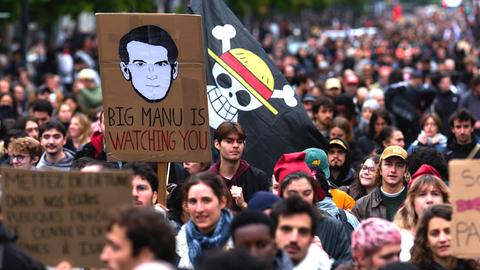 Demonstranten ziehen mit Plakaten, darunter eines mit dem Porträt des französischen Präsidenten Macron und der Aufschrift "Big Manu is watching you", in Richtung Porte d'Italie.