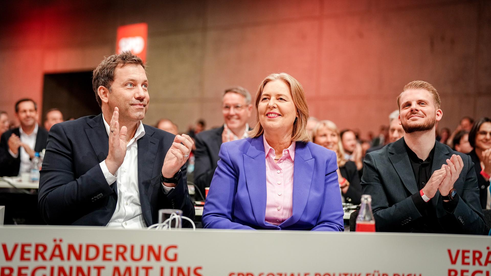 Die drei sitzen an einem Tisch beim SPD-Parteitag nebeneinander und klatschen.