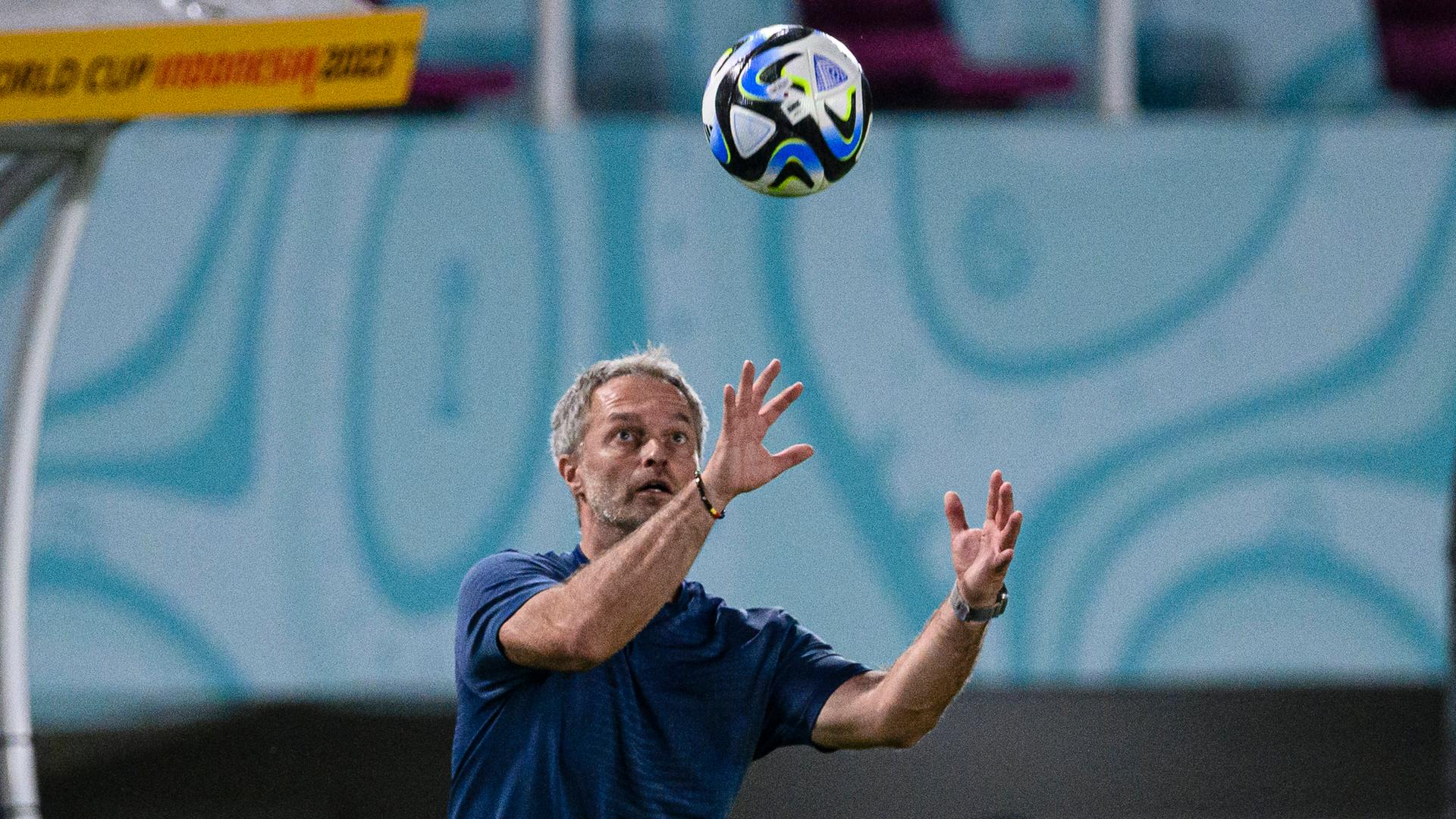 Ein Mann im Polohemd blickt auf einen Fußball. Dieser befindet sich in der Luft.