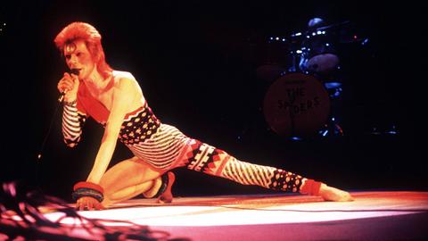 Sänger David Bowie während eines Konzerts in London auf der Bühne, nach vorne gestreckt, knieend. Sänger David Bowie während eines Konzerts in London auf der Bühne, nach vorne gestreckt, knieend.