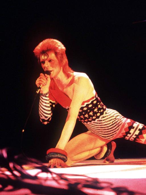 Sänger David Bowie während eines Konzerts in London auf der Bühne, nach vorne gestreckt, knieend.
