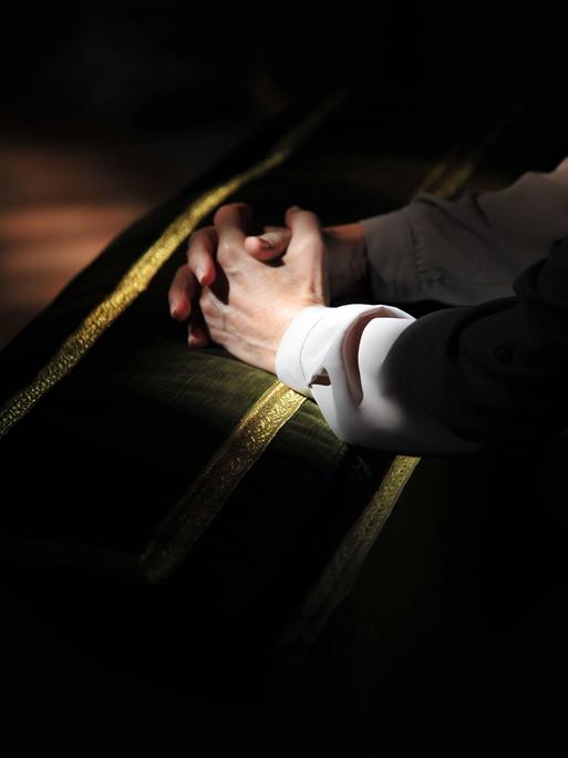 Auf einer Kirchenbank liegen die zum Gebet gefalteten Hände eines jungen Mannes.