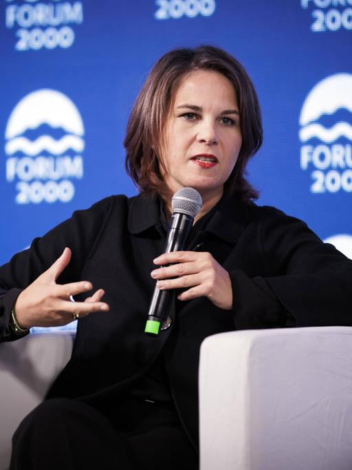 Außenministerin Baerbock hält ein Mikrofon und gestikuliert. Im Hintergrund sieht man das Logo des Forum 2000, das die Podiumsdiskussion in Prag organisiert hat.