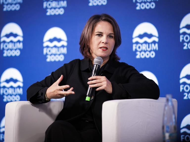 Außenministerin Baerbock hält ein Mikrofon und gestikuliert. Im Hintergrund sieht man das Logo des Forum 2000, das die Podiumsdiskussion in Prag organisiert hat.