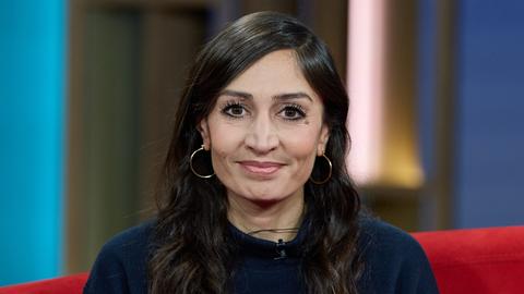 Die Journalistin und Autorin Gilda Sahebi sitzt  vor der Ausstrahlung von DAS! Rote Sofa, einer Live-Talksendung des Norddeutschen Rundfunks (NDR), auf einem roten Sofa und lächelt in die Kamera.