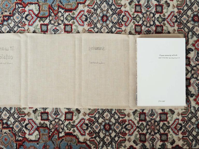 Das Buch liegt auf einem Teppich. Der Umschlag aus ausgefranstem Leinen ist vom gebundenen Buch abgelöst und liegt unter dem Buch auf dem Teppich.