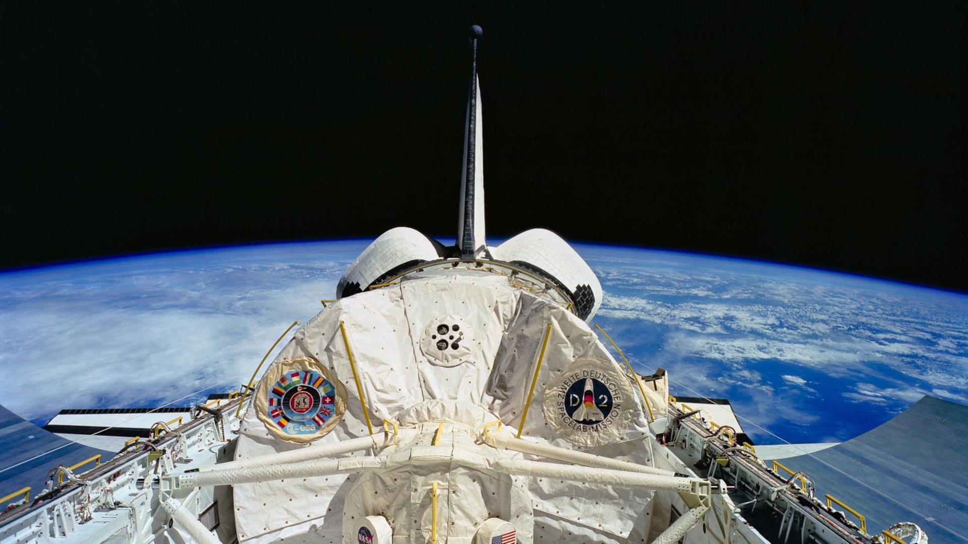Blick aus einem im Weltraum fliegenden Space Shuttle auf den vorderen Teil des Raumschiffs und auf den gekrümmten Horizont der Erde. 
