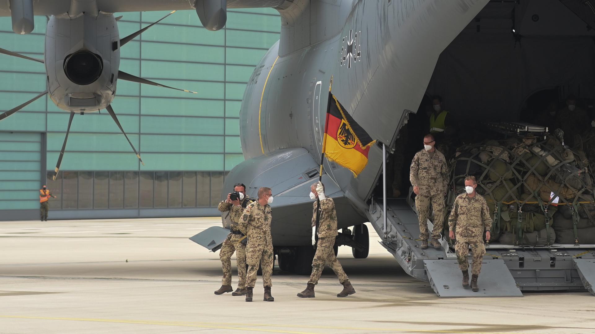 Soldaten der Bundeswehr steigen mit ihrer Truppenfahne aus einen Transportflugzeug.