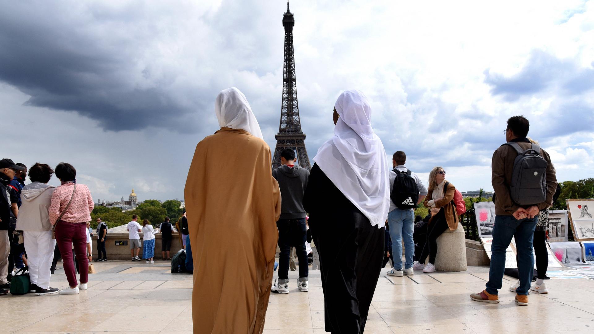 Zwei Frauen in Abayas – den langen arabischen Übergewändern – von hinten vor dem Eifelturm in Paris