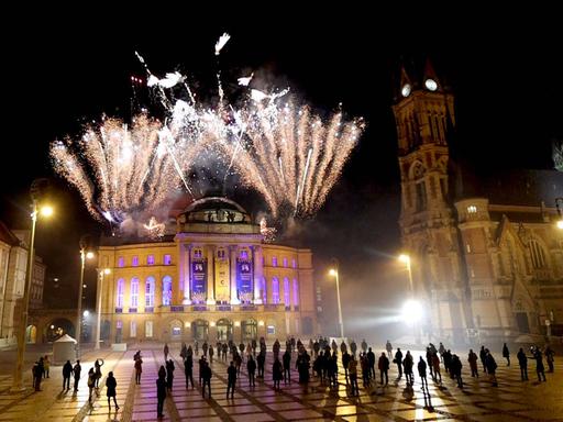 Blick auf den bevölkerten Vorplatz vor dem Chemnitzer Opernhaus, über dem ein buntes Feuerwerk aufscheint.
