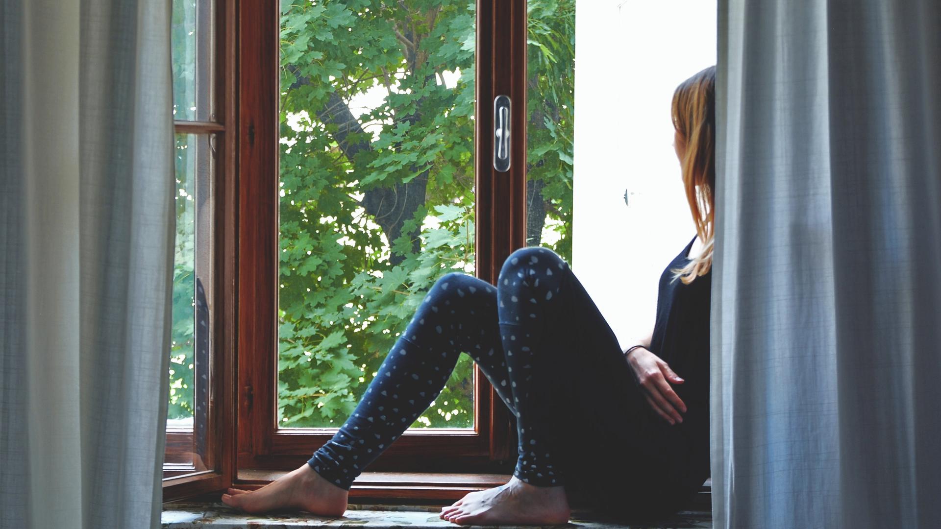 Eine Frau sitzt auf einem Fensterbrett und schaut nach draußen.