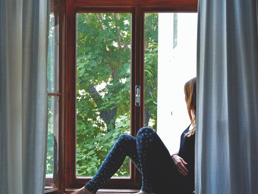 Eine Frau sitzt auf einem Fensterbrett und schaut nach draußen.