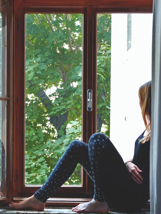 Eine Frau sitzt auf einem Fensterbrett und schaut nach draußen.