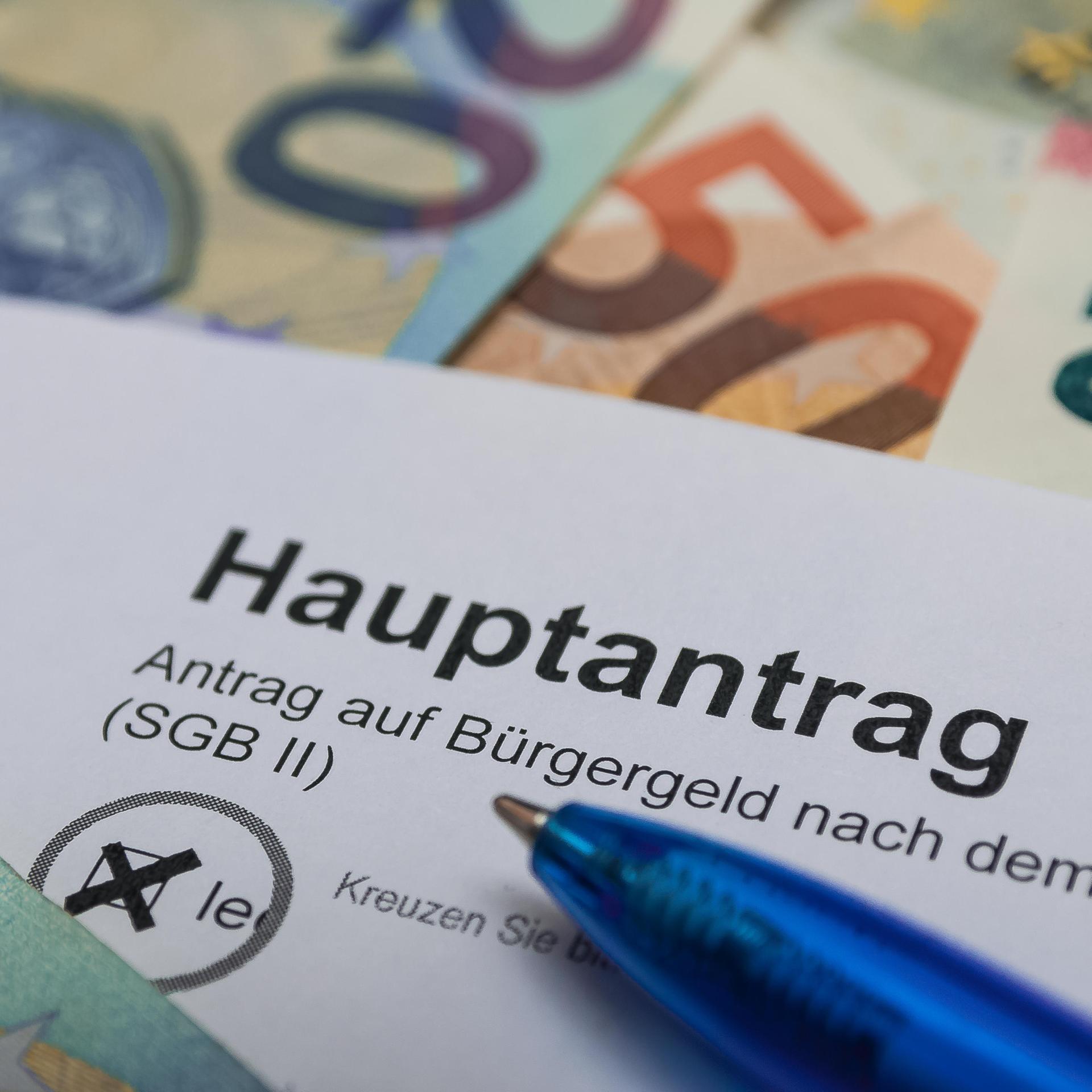 Ein Antrag auf Bürgergeld mit einem Kugelschreiber, dahinter mehrere Euro-Scheine