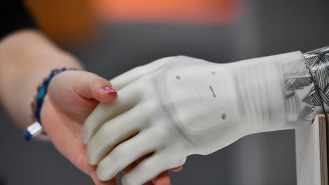 Eine Schülerin greift bei einer Ausstellung nach der künstlichen Hand eines Roboters.