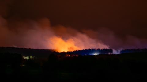 Ein Waldbrand erhellt den Himmel während Rauch aufsteigt. 