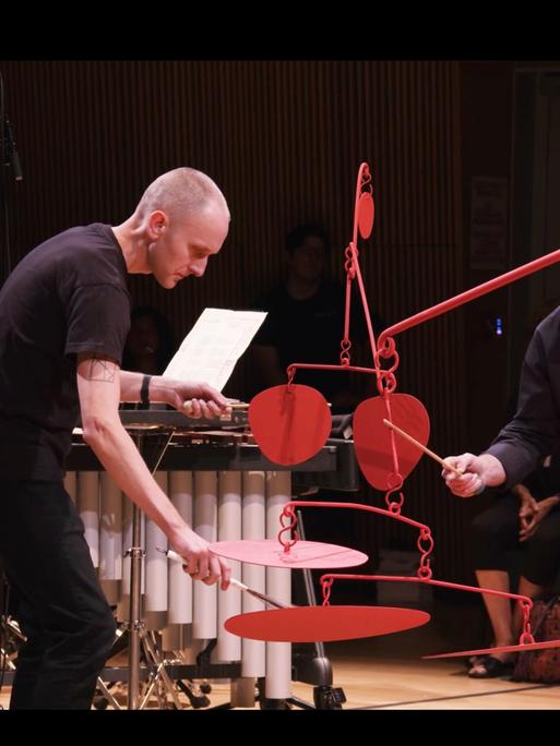 Zwei Musiker des Talujon Percussion Quartets bespielen eine rote bewegliche Skulptur des Amerikanischen Künstlers Alexander Calder