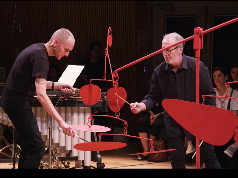 Zwei Musiker des Talujon Percussion Quartets bespielen eine rote bewegliche Skulptur des Amerikanischen Künstlers Alexander Calder