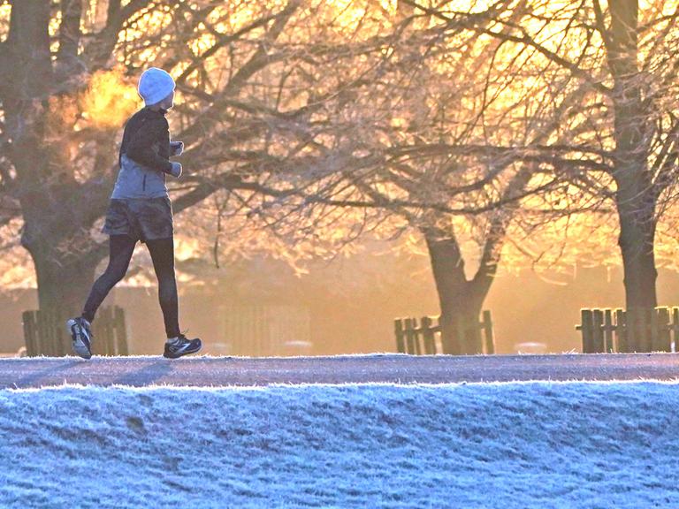 Ein Jogger ist im Winter bei Sonnenaufgang im Park unterwegs. 
