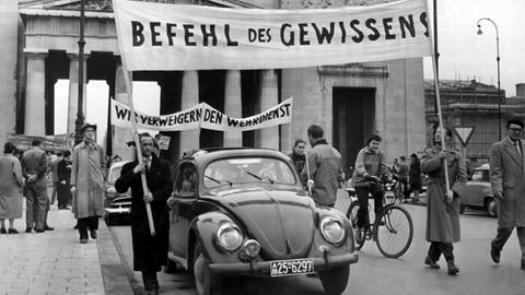 Demonstrationszug gegen den Wehrdienst: Männer tragen Transparente mit der Aufschrift "Befehl des Gewissens" und "Wir verweigern den Wehrdienst", aufgenommen vor den Propyläen am Münchner Königsplatz am 24. März 1956.