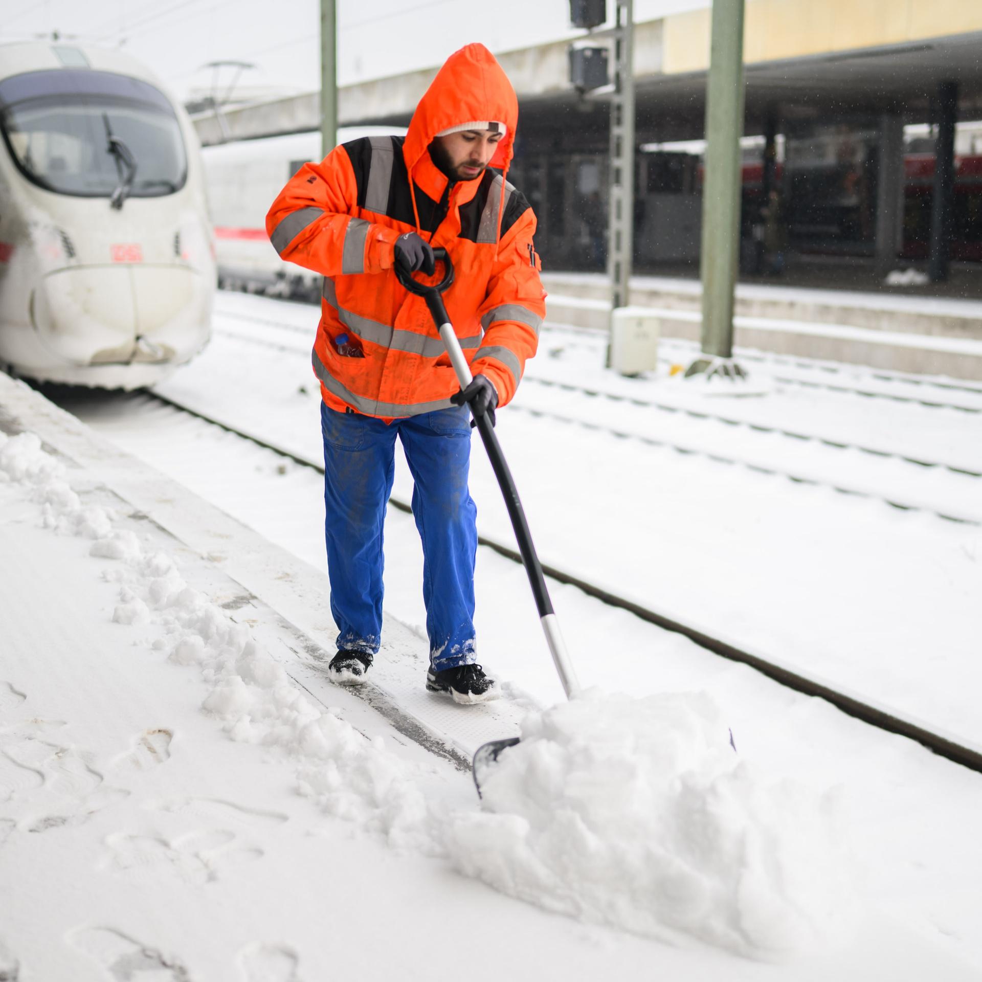 Mitarbeiter befreien Bahnsteige vom Schnee neben einem stehenden ICE der Deutschen Bahn im Hauptbahnhof Hannover. 