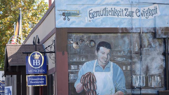 Ein Wandbild im texanischen New Braunfels wirbt für ein deutsches Restaurant. Das Bild zeigt einen Koch, der Würstchen zubereitet, darüber der Schriftzug: Gemütlichkeit zur Ewigkeit. 