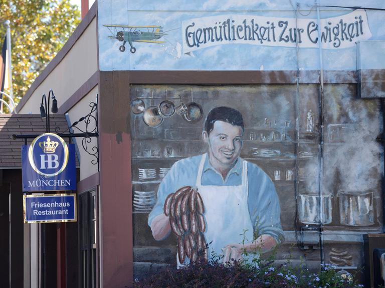 Ein Wandbild im texanischen New Braunfels wirbt für ein deutsches Restaurant. Das Bild zeigt einen Koch, der Würstchen zubereitet, darüber der Schriftzug: Gemütlichkeit zur Ewigkeit. 