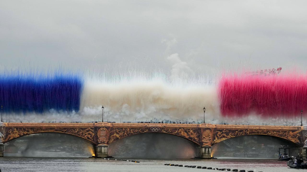 Die Pont d'Austerlitz über der Seine in Paris mit goldenen Applikationen. Darüber zeigen während der Eröffnungsfeier Rauchbomben die französische Nationalflagge.