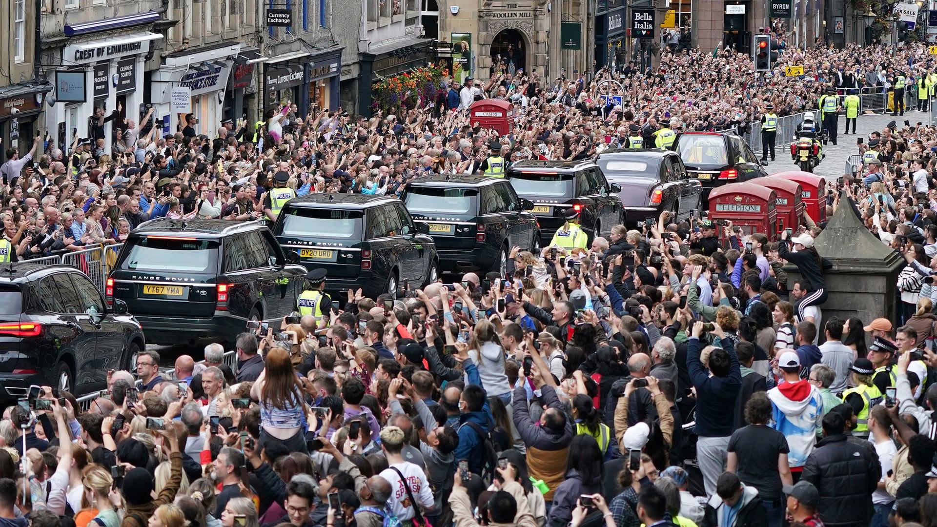 In Edinburgh stehen tausende Menschen am Straßen-Rand. Sie sehen Autos mit dem Sarg von Königin Elisabeth vorbei fahren.