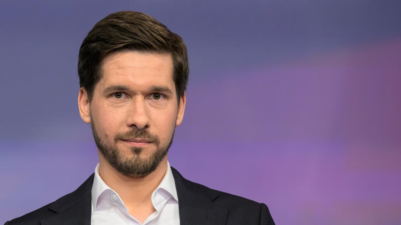 Vassili Golod steht vor einem farbigen Hintergrund. Er trägt Vollbart, ein schwarzes Jackett und ein weißes Hemd. 
