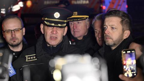 Mehrere Männer stehen im Dunklen vor Kameras. Ein Mann in Uniform gibt Interviews.