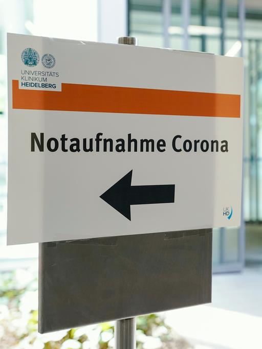 Eine Frau kommt aus einem Krankenhaus, im Vordergrund ist ein Schild mit der Aufschrift "Notaufnahme Corona" zu sehen