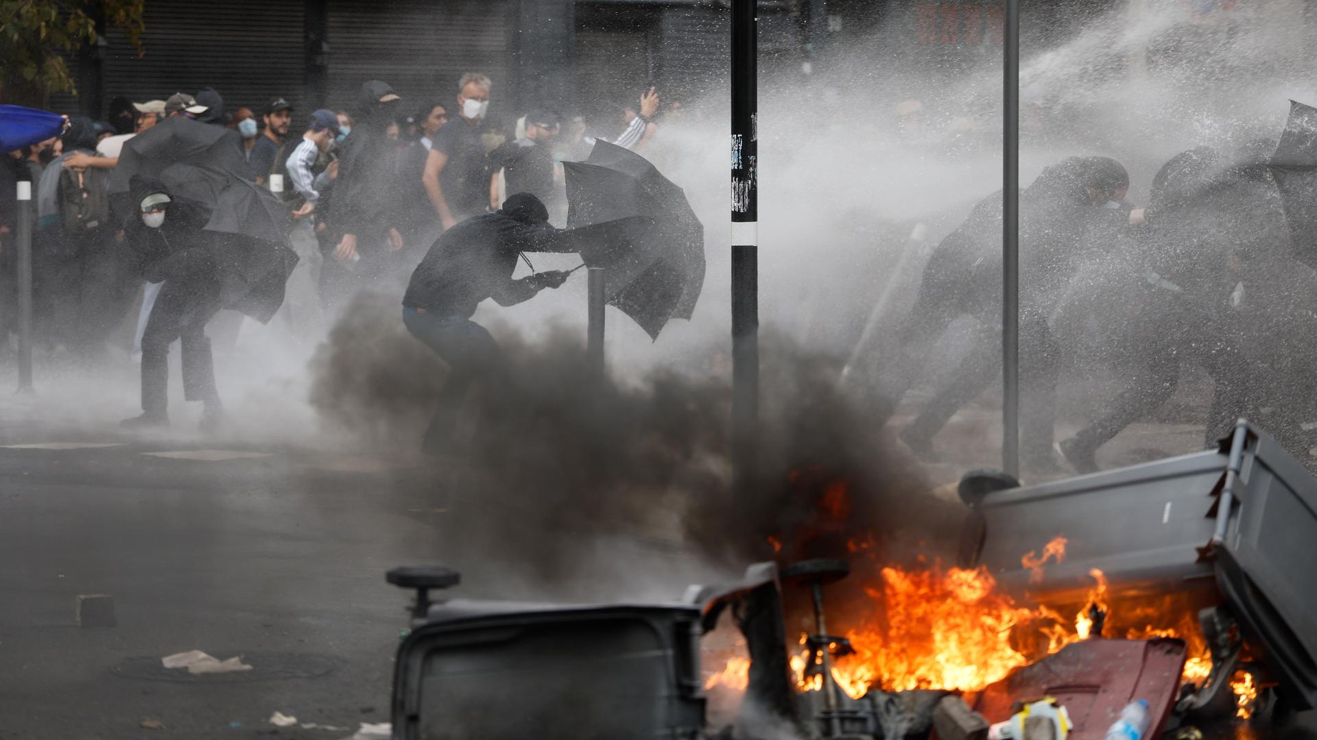 Demonstranten gehen hinter Regenschirmen vor einem Wasserwerfer in Deckung. Demonstranten gehen hinter Regenschirmen vor einem Wasserwerfer in Deckung.