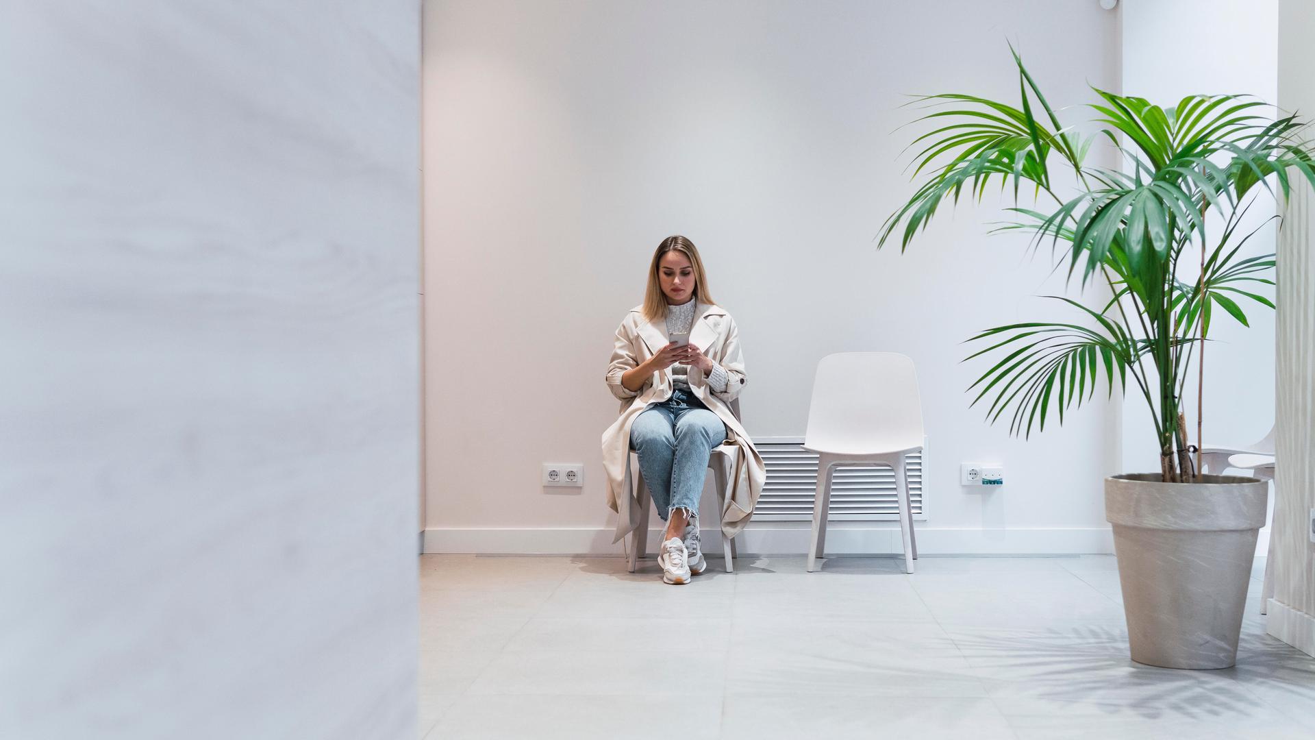 Eine junge Frau sitzt im Wartezimmer einer Arztpraxis und schaut auf ihr Handy.