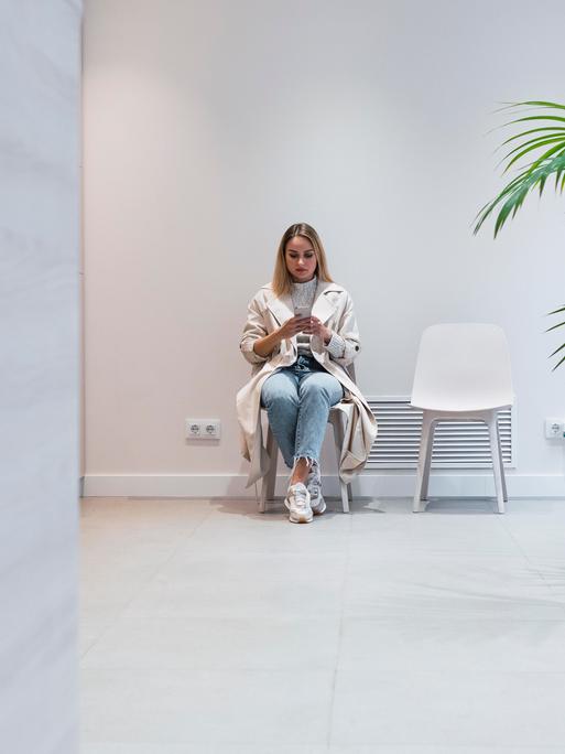 Eine junge Frau sitzt im Wartezimmer einer Arztpraxis und schaut auf ihr Handy.