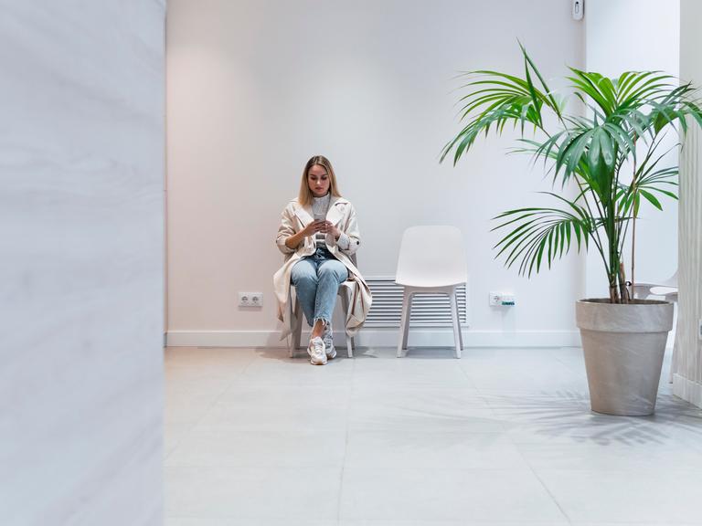 Eine junge Frau sitzt im Wartezimmer einer Arztpraxis und schaut auf ihr Handy.