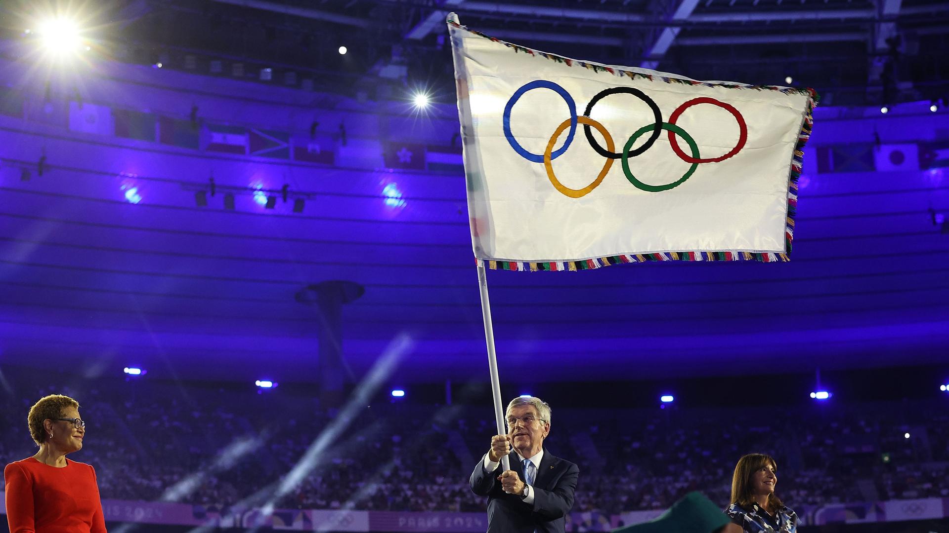 Thomas Bach schwenkt bei der Abschlussfeier der Olympischen Spiele in Paris die Olympische Fahne.