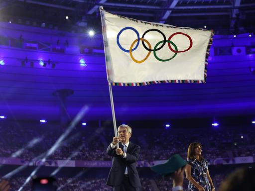 Thomas Bach schwenkt bei der Abschlussfeier der Olympischen Spiele in Paris die Olympische Fahne.