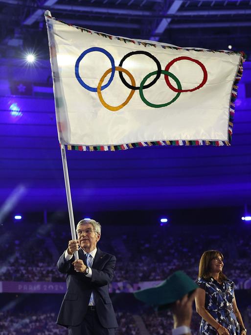 Thomas Bach schwenkt bei der Abschlussfeier der Olympischen Spiele in Paris die Olympische Fahne.