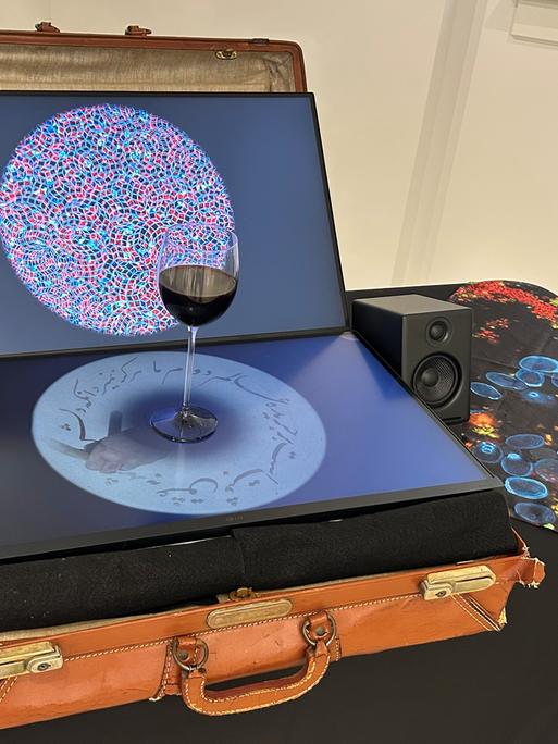 Eine Komposition aus einem alten Lederkoffer, darauf ein geöffneter Laptop mit einem Glas Rotwein
