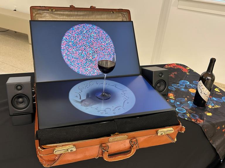 Eine Komposition aus einem alten Lederkoffer, darauf ein geöffneter Laptop mit einem Glas Rotwein