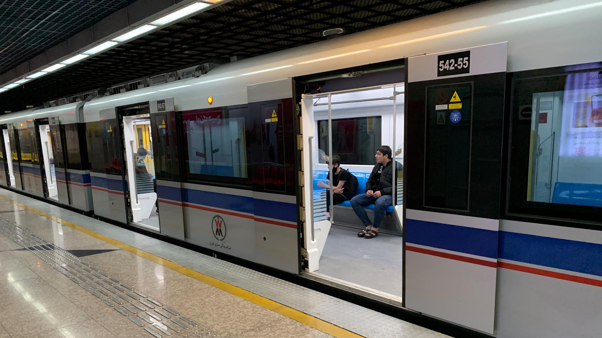 Die U-Bahn steht an einem Bahnsteig. Durch zwei geöffnete Türen sieht man drei Fahrgäste.