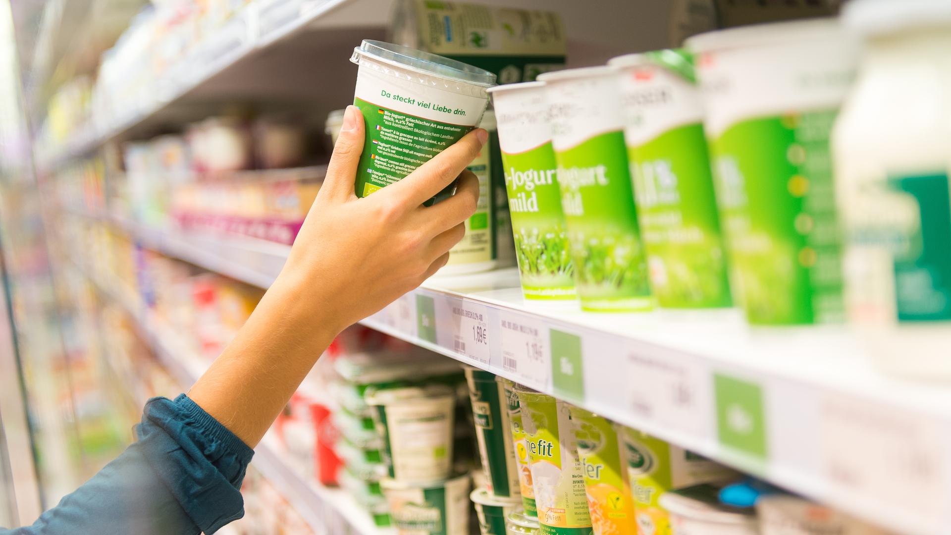 Eine Hand greift einen Joghurtbecher aus dem Supermarksregal. Eine Hand greift einen Joghurtbecher aus dem Supermarksregal.